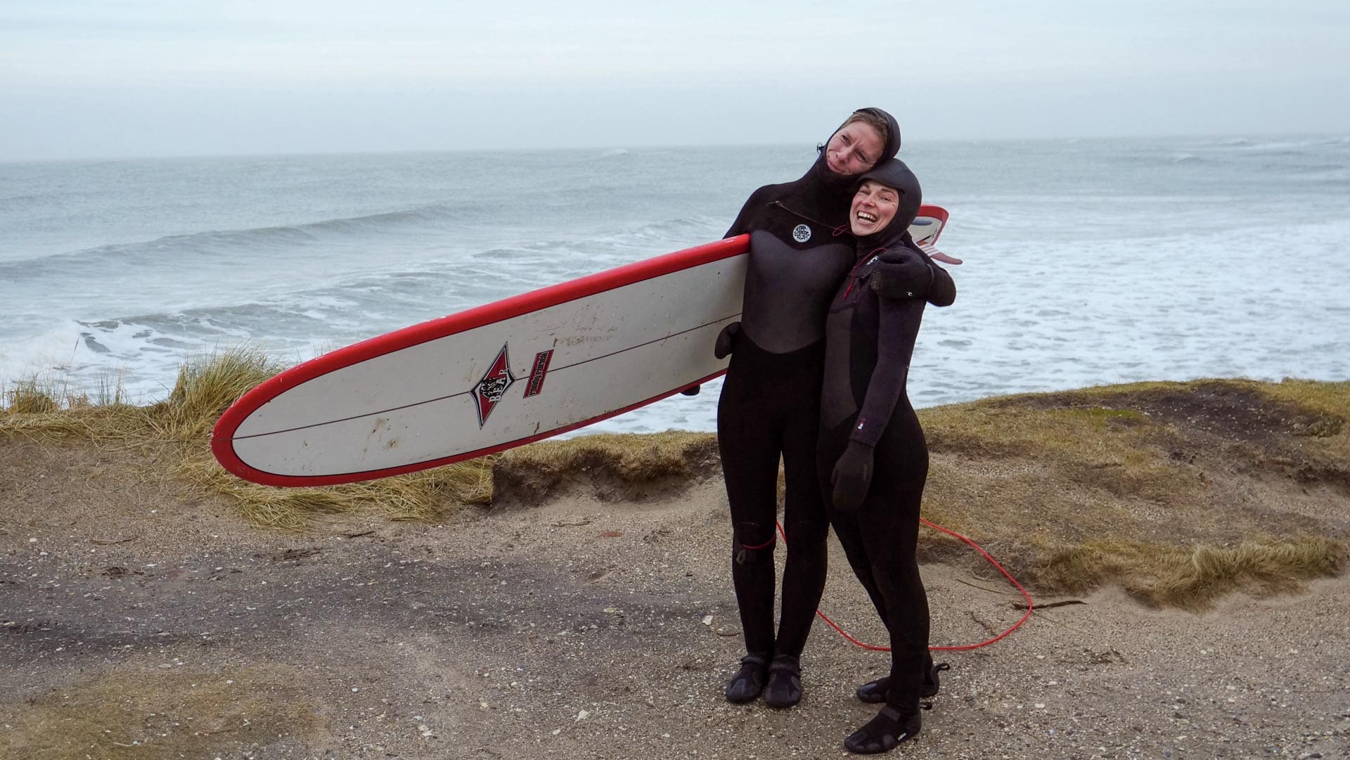 2 Frauen am Strand mit Surfbrett unterm Arm